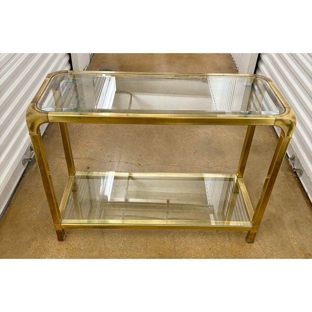 Stunning Hollywood Regency Brass Console in the style of Mastercraft. An inset glass top and bottom shelf provide a...