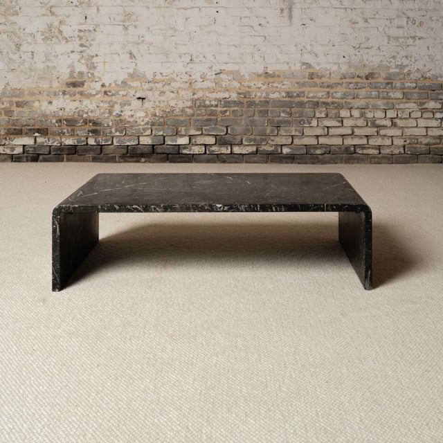 A 1970s French coffee table featuring a substantial rectangular top in dark marble with natural veining. The piece is...