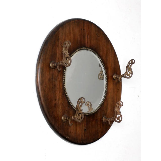 This antique hall mirror features a wood frame with four brass hooks and a beveled glass center, accented by brass nail...