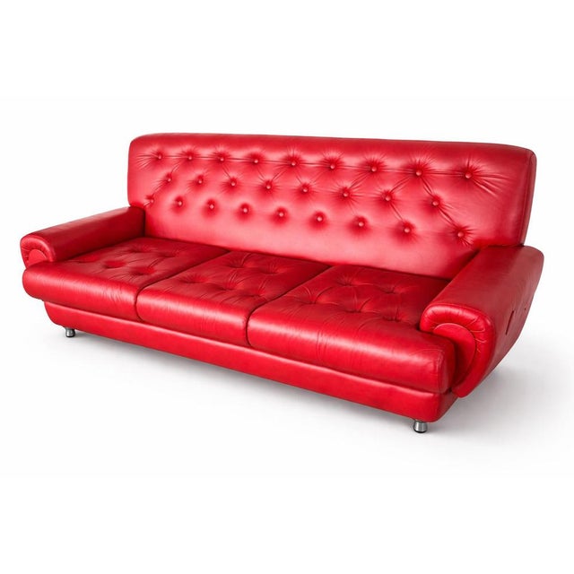 A striking vintage three-seater sofa upholstered in vibrant red leather, featuring classic deep button tufting across the...