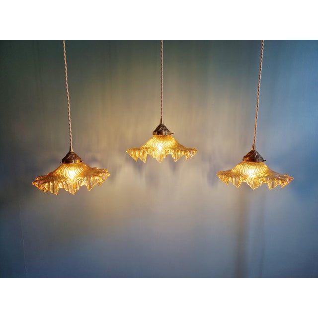 Trio of amber-colored scalloped glass pendant lights with iridescent reflections and brass claws, 1930s. Each pendant...