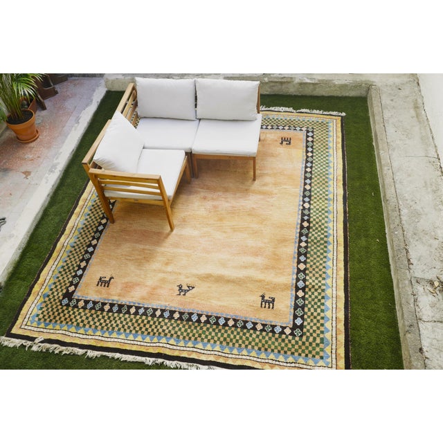 Hand-knotted Gabbeh wool rug made in India with a warm peach-orange, geometric and checkered border and animal motifs. One...