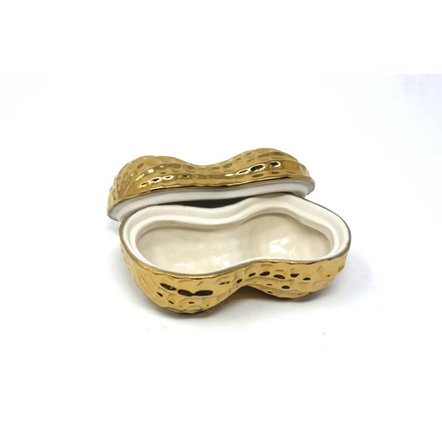 A vintage lidded box in the form of an oversized peanut, decorated with metallic gold finish.