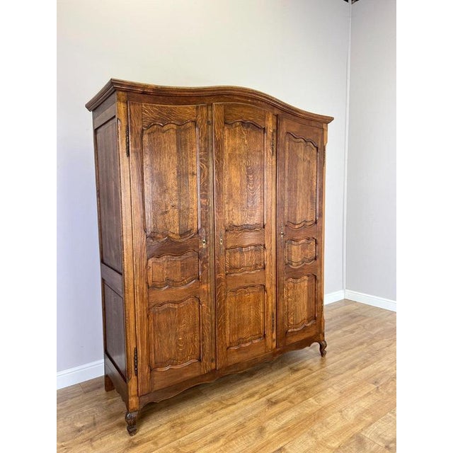 An elegant Vintage French Louis wardrobe featuring a warm oak finish, three panelled doors, a gently curved top and...