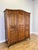 An elegant Vintage French Louis wardrobe featuring a warm oak finish, three panelled doors, a gently curved top and...