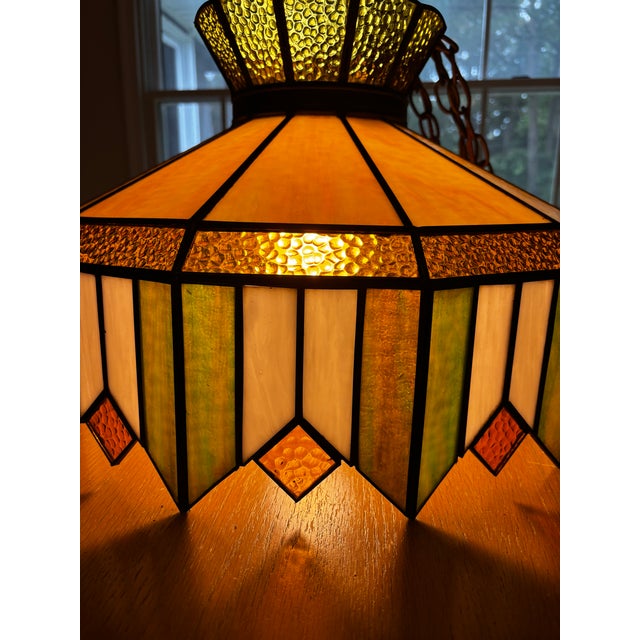 Vintage hanging light featuring rich green, gold, amber and ivory panels with decorative metal trim. A true mid century...