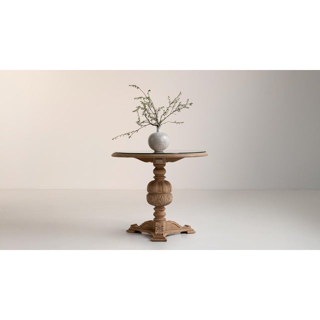 A decorative table featuring carved detailing inspired by Neo-Renaissance forms, paired with a glass top that allows the...