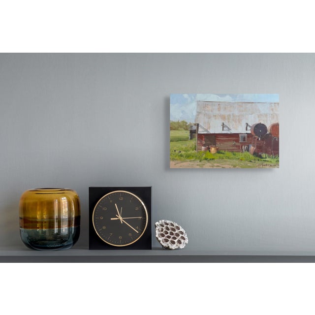 This oil painting depicts a rustic barn, its weathered red exterior contrasting with the vibrant greens of the surrounding...