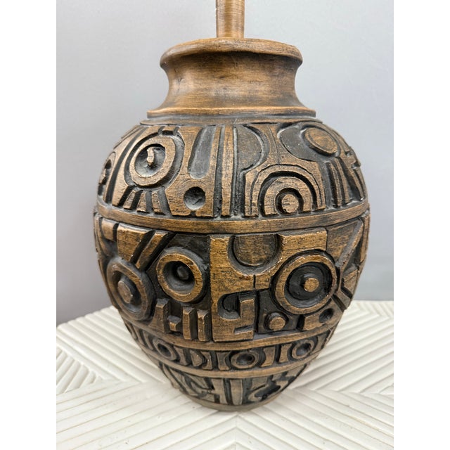 Mid-century sculptural terracotta table lamp featuring a bold, carved relief body with graphic, abstract motifs and a warm...