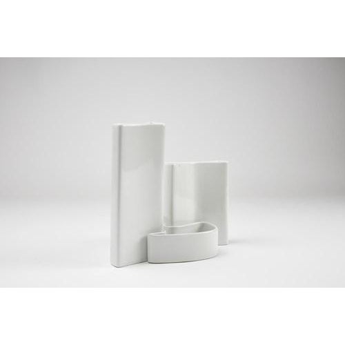 A flower vase centerpiece made of white glazed ceramic, consisting of three interlocking pieces. Manufacturer’s label on...
