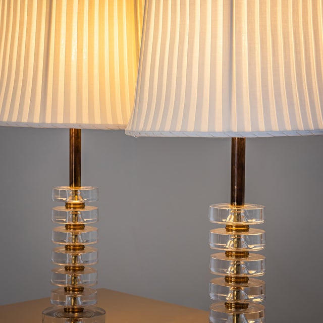 Pair of table lamps with bases composed of clear glass discs and brass elements. The table lamps are fitted with white...