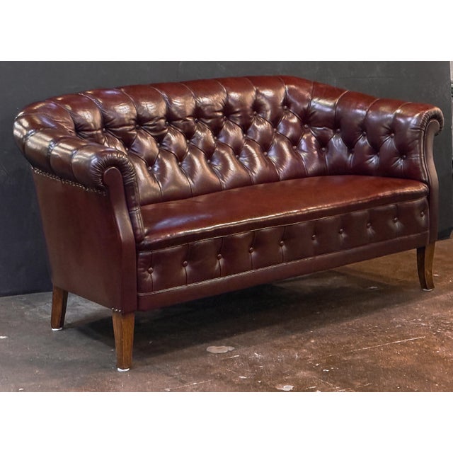 A handsome Swedish sofa or settee of tufted oxblood leather in the Chesterfield style, featuring a gently arching...
