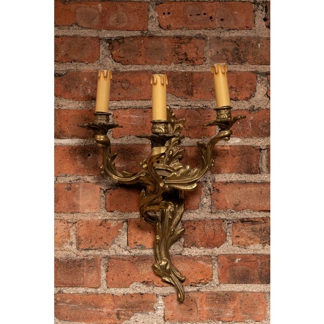 Decorative pair of cast metal wall sconces in a Rococo revival style, featuring elaborate scrolling acanthus leaf forms...