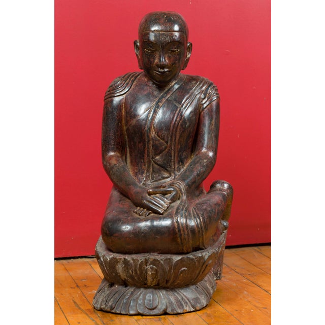 A Thai hand carved lacquered wood sculpture from the 18th century depicting a seated monk. Created in Thailand during the...