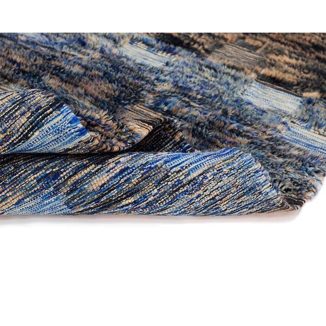 Timeless hand-knotted wool rug displaying a mesmerizing pattern featuring shades of blues and earthy tans, reminiscent of...