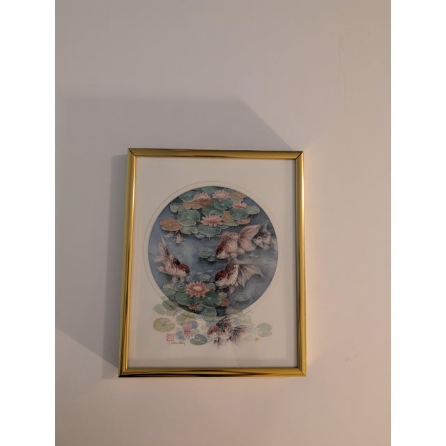 This artwork is a hand-signed limited edition print by artist John Cheng, featuring fantail goldfish swimming among pink...