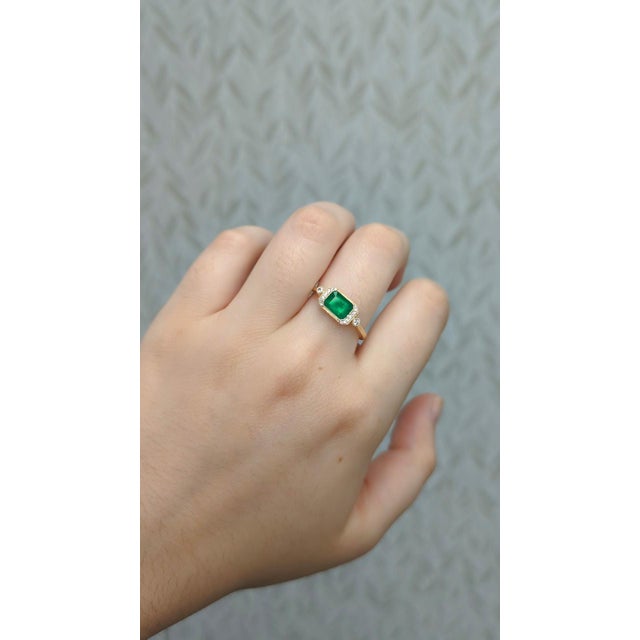 This refined ring showcases a 0.38ct emerald-cut Colombian emerald (7x5mm), prized for its vibrant green hue and...