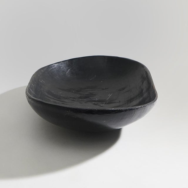 A black ebonized wooden bowl produced in the 1960s, distinguished by an organic form that appears to have been shaped...