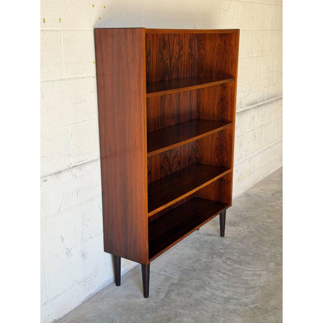 This open bookcase features a streamlined silhouette with four spacious shelves. It stands on tapered black legs that...