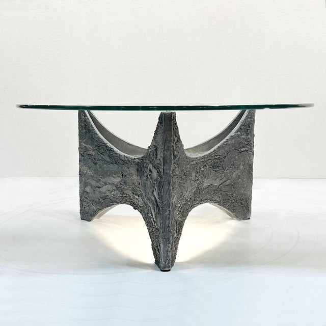 Brutalist coffee table with triangular formed base, cast in aluminium with a round glass top. Underneath the base is...