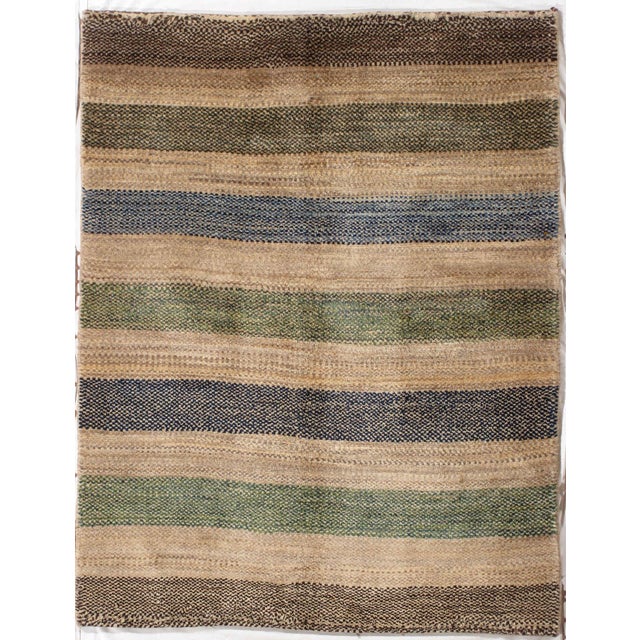 Persian hand-knotted Lori Gabbeh wool rug featuring horizontal bands in earthy tones of beige, brown, green, and blue. The...
