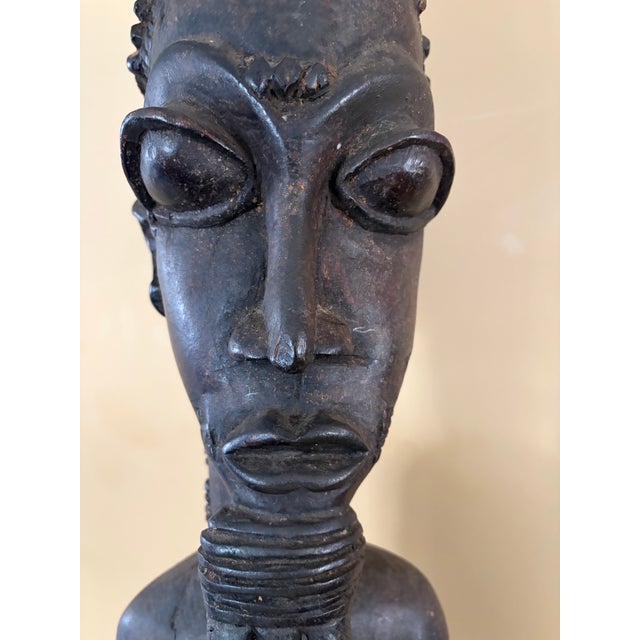 20th century male Baule figure sitting on a stool. This vintage figure is made of wood. It is brown in color. It shows...