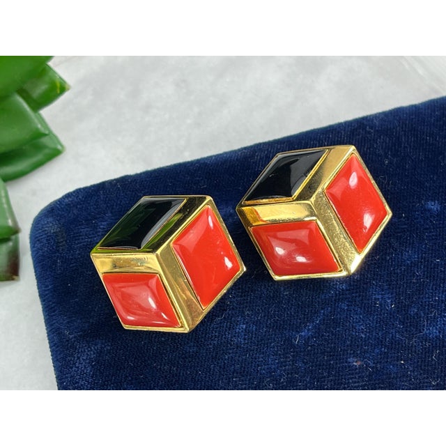 A pair of vintage costume jewelry earrings, featuring orange and black enamel on gold tone metal. The earrings look like...