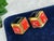 A pair of vintage costume jewelry earrings, featuring orange and black enamel on gold tone metal. The earrings look like...
