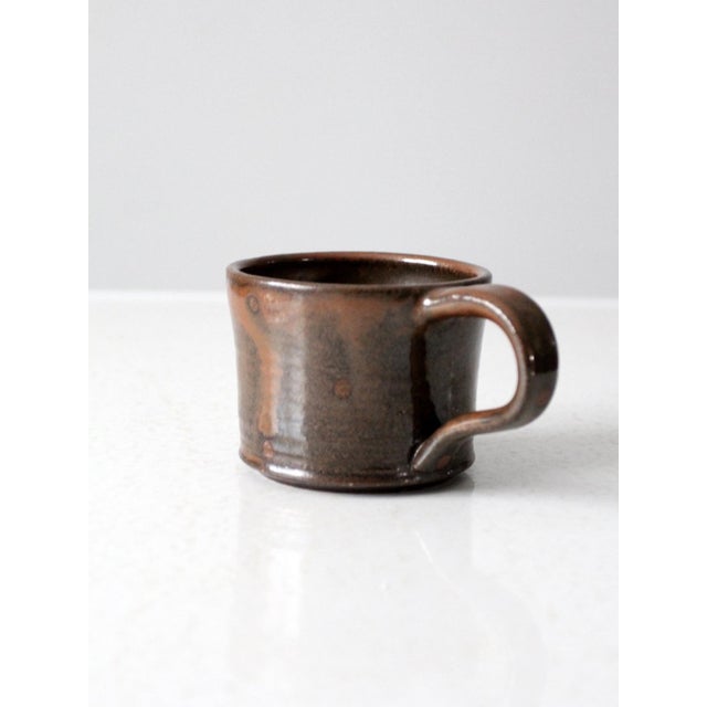 This vintage studio pottery mug features a deep brown glaze accented by a contrasting drip glaze at the rim and subtle...