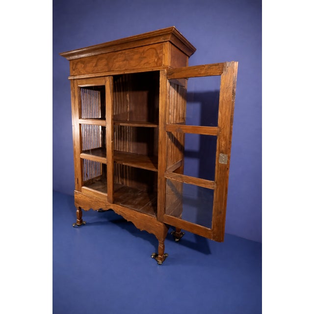 Antique wooden display cabinet featuring glass-paneled doors, slatted side details, and a decorative crown top. Wheels not...