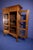 Antique wooden display cabinet featuring glass-paneled doors, slatted side details, and a decorative crown top. Wheels not...