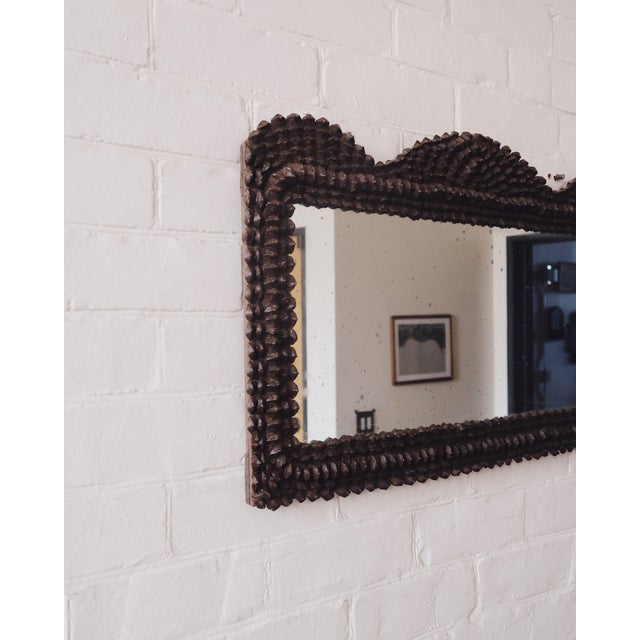 A vertically oriented wall mirror with a fully wrapped pinecone frame, built from densely applied natural elements over a...