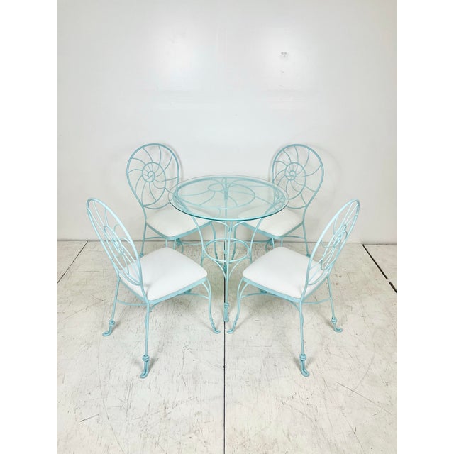 Wrought iron nautilus shell dining set. Four bistro chairs with round table base with glass top. Newly refinished in a...