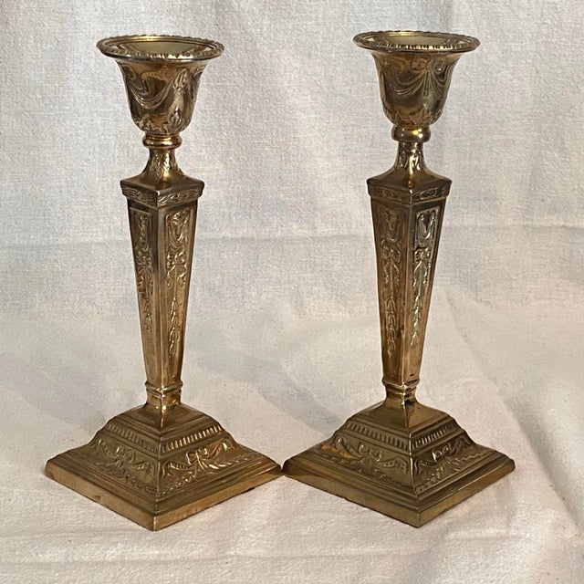 These candle holders feature ornate ram's head and ribbon motifs on tapered stems with square bases.