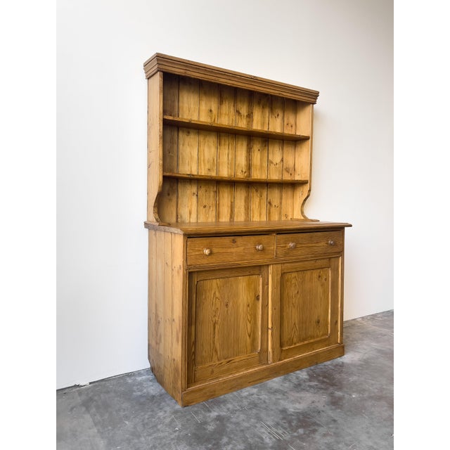 This antique English pine hutch kitchen dresser features a top shelf or plate rack with traditional cup hooks, perfect for...
