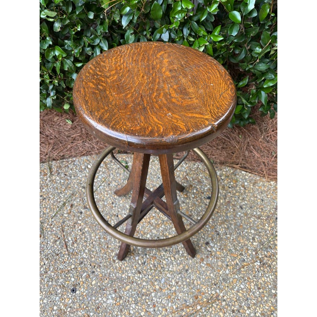 Iconic early twentieth century industrial drafting stool in nicely-distressed solid wood with beautifully-aged heavy brass...