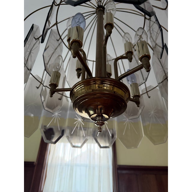 Striking vintage 1970s Hollywood Regency chandelier featuring a brass-tone frame adorned with faceted smoked glass prism...