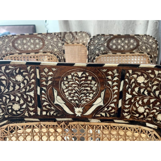 This is an intricately decorated armchair featuring an elaborate bone or mother-of-pearl inlay pattern across the dark...