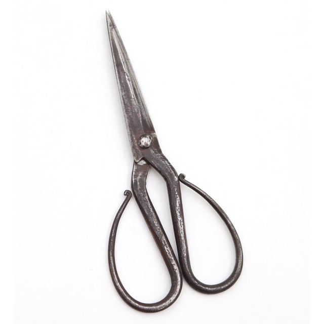 Vintage steel scissors with a distressed black finish. It features continuous loop handles and a riveted pivot joint,...
