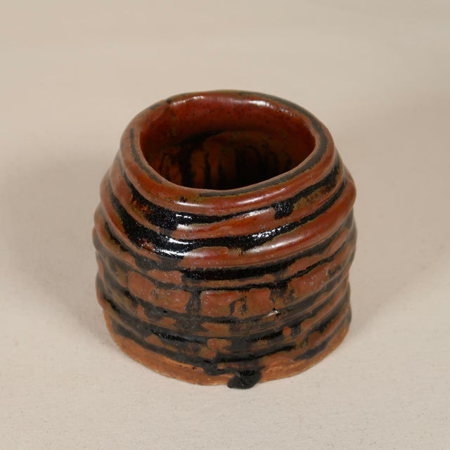 This hand-thrown studio pottery vessel features a compact, cylindrical form with pronounced horizontal ribbing, giving it...