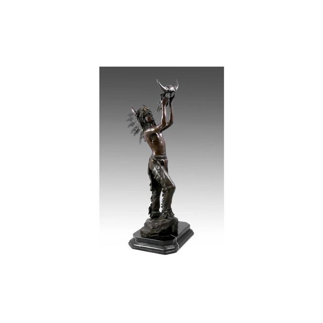 This bronze sculpture depicts a Native American in an upright, dignified pose, wearing the traditional attire of the North...