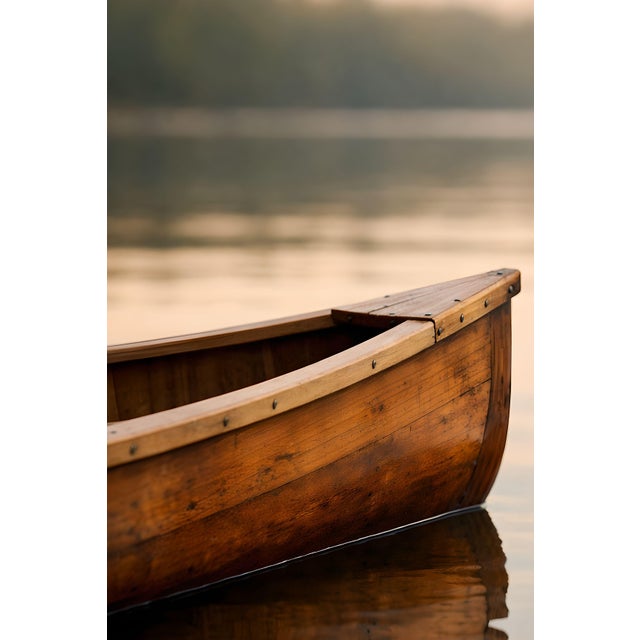 Minimalist lake artwork featuring a wooden canoe resting on calm water with soft reflections and warm, natural tones. The...