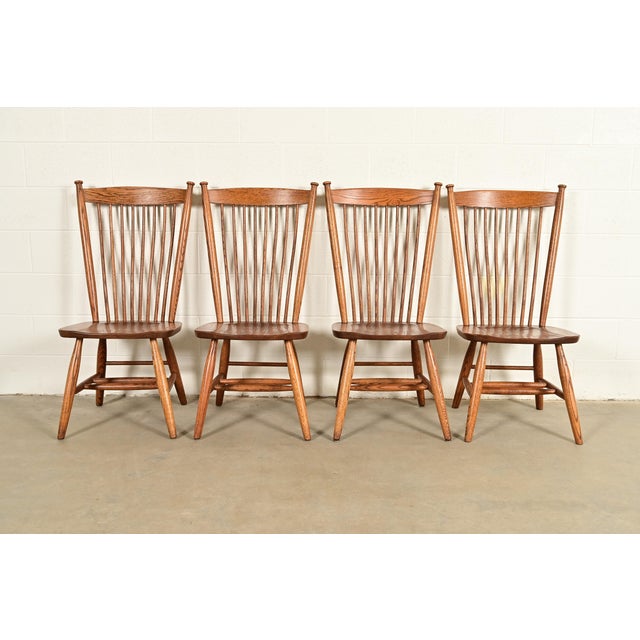 A gorgeous set of four American Colonial or Arts & Crafts style solid oak spindle back Windsor dining chairs In the manner...
