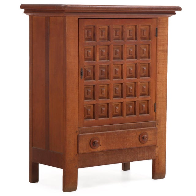 This cabinet having a single paneled door richly decorated with a grid of 25 deeply recessed, geometric square panels,...