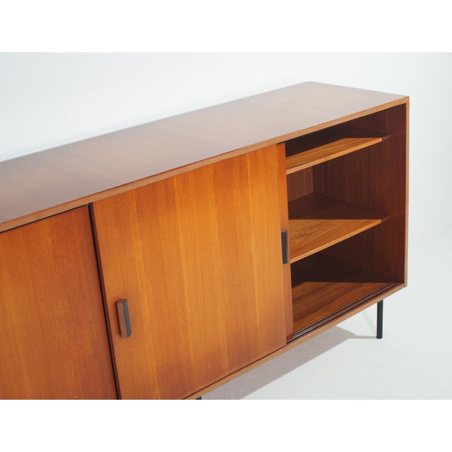 An original 1950s teak wood sideboard with three sliding doors, black metal legs and handles created by ISA Bergamo. This...