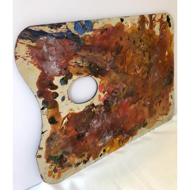 Beautiful vintage artist’s palette covered in dried oil paint. The paint is composed of mostly warm earth tones and...