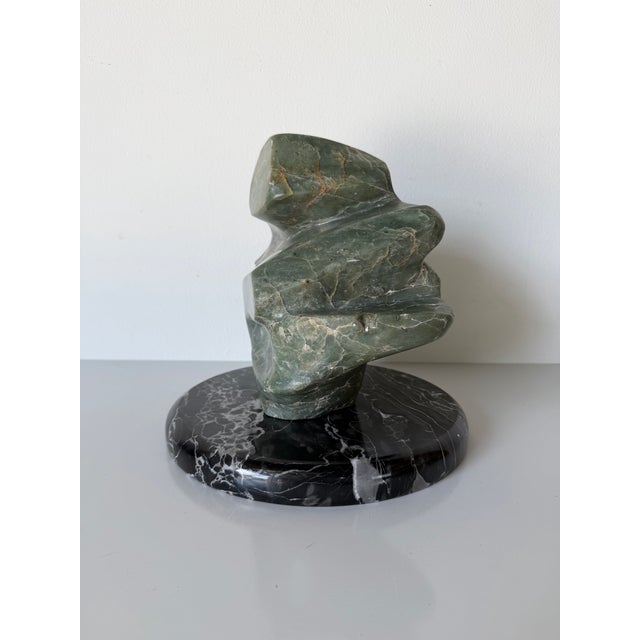 A striking 1980s vintage abstract sculpture hand-carved from richly veined green marble and displayed on a polished black...