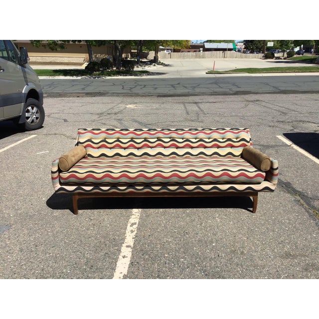 Striking vintage sofa featuring a long, streamlined silhouette with gently rolled arms, tapered wood legs, and a button-...