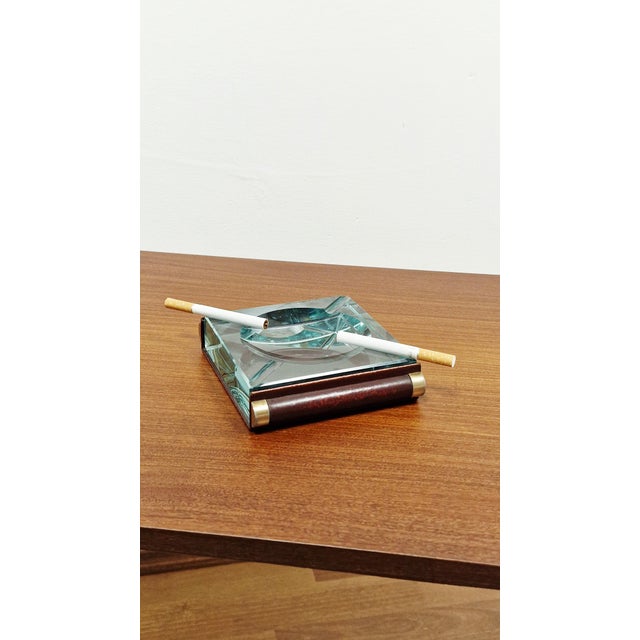 The ashtray was made of thick crystal, often described as "Nile green." It has a square shape with a hollowed-out and...