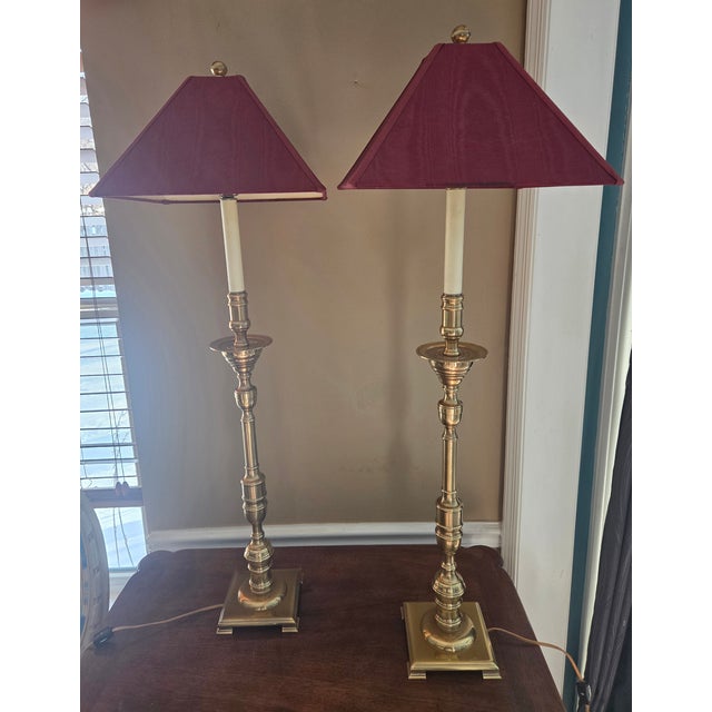A pair of impressive brass candlestick lamps by Frederick Cooper of Chicago. Original red silk moire' fabric shades are...